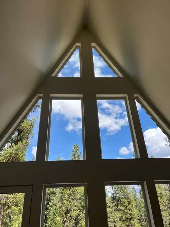 Triangular window framing a bright blue sky with fluffy clouds, overlooking green trees.