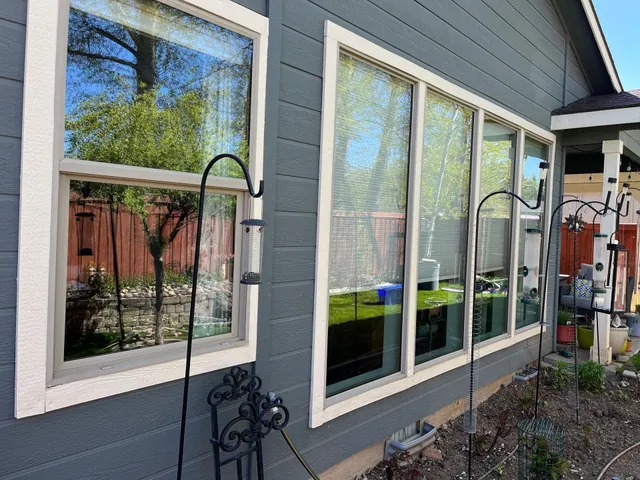 Exterior view of a house with windows reflecting a tree and a red fence; bird feeders stand outside.
