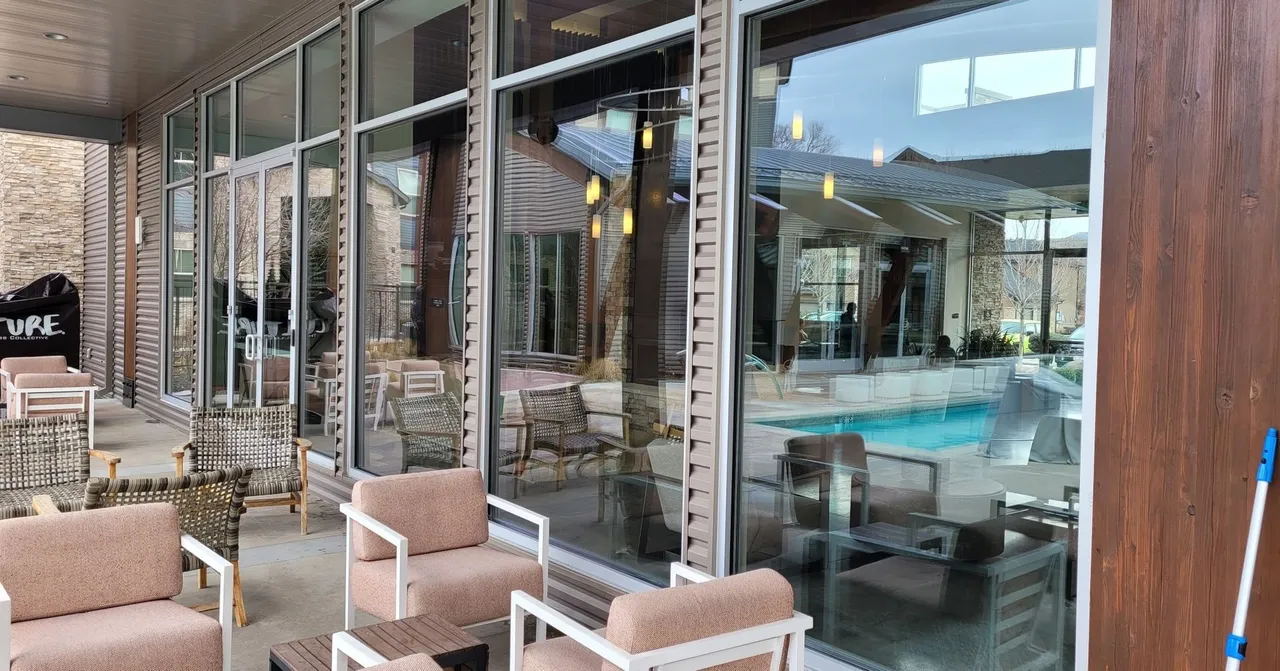 Outdoor patio with seating and large glass windows reflecting a pool and surrounding building.